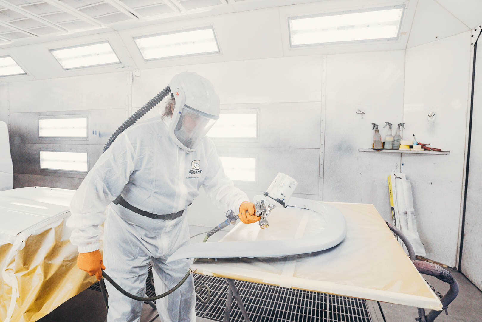 Close up of automotive painter in white suit painting vehicle parts with spray gun.