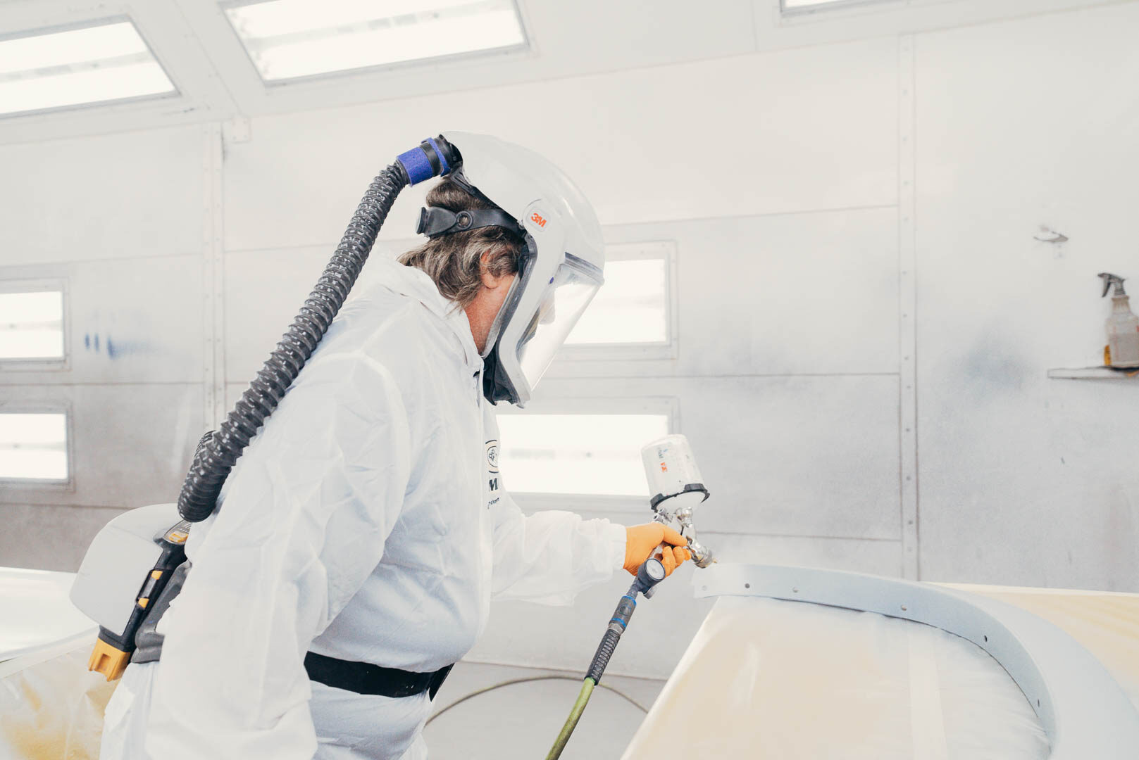 Close up of automotive painter in white suit painting vehicle parts with spray gun.