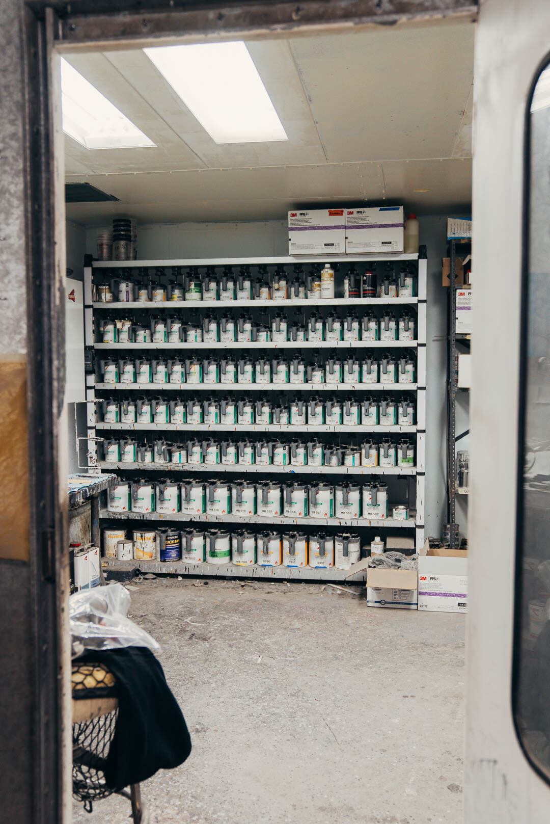 A shelf full of different automotive paints with door open in foreground