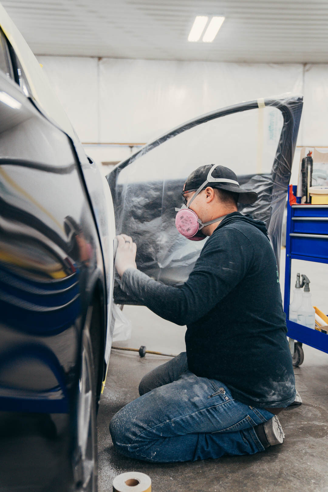 Lander's employee with a painting facemask, sanding down the black vehicle before painting